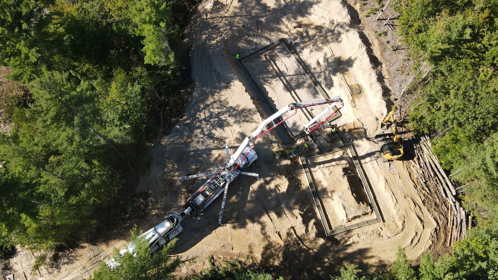 Aerial of a concrete pump truck pouring a foundation on a wooded site
