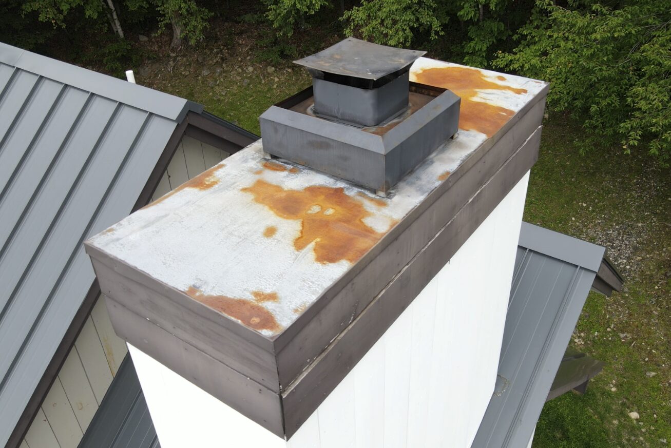 Aerial inspection of a metal chimney cap showing rust and corrosion